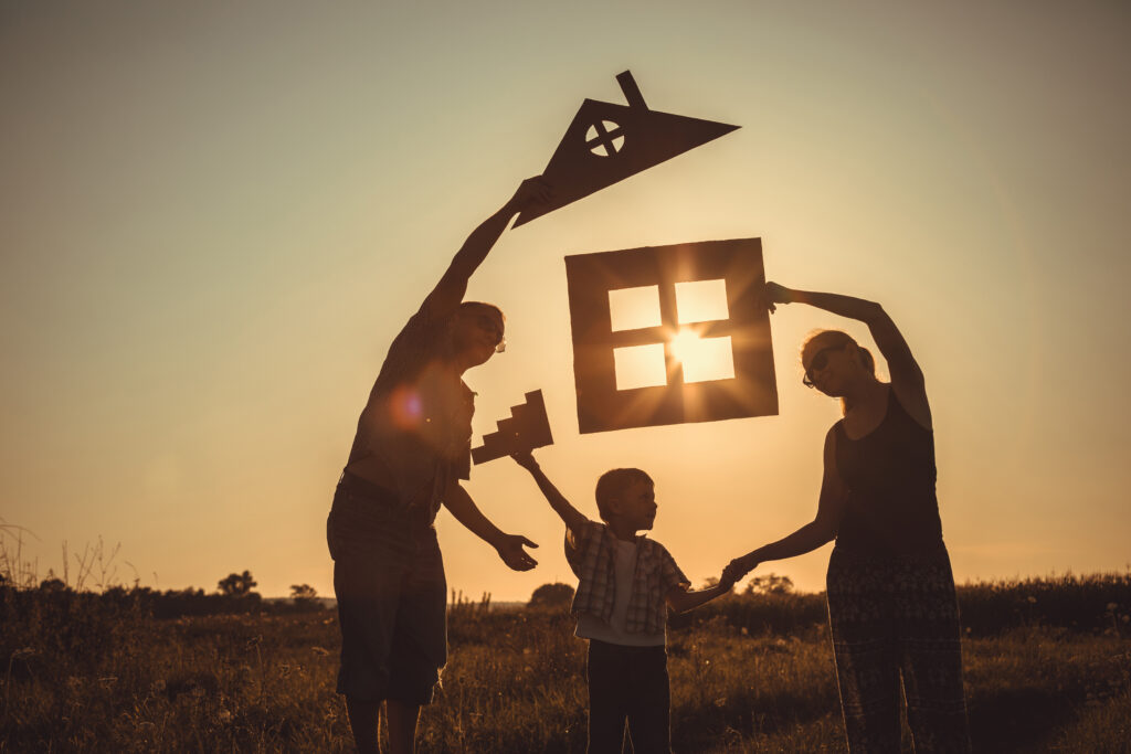 Happy family standing on the field at the sunset time. Family is holding cutouts of a house concept in silhouette.